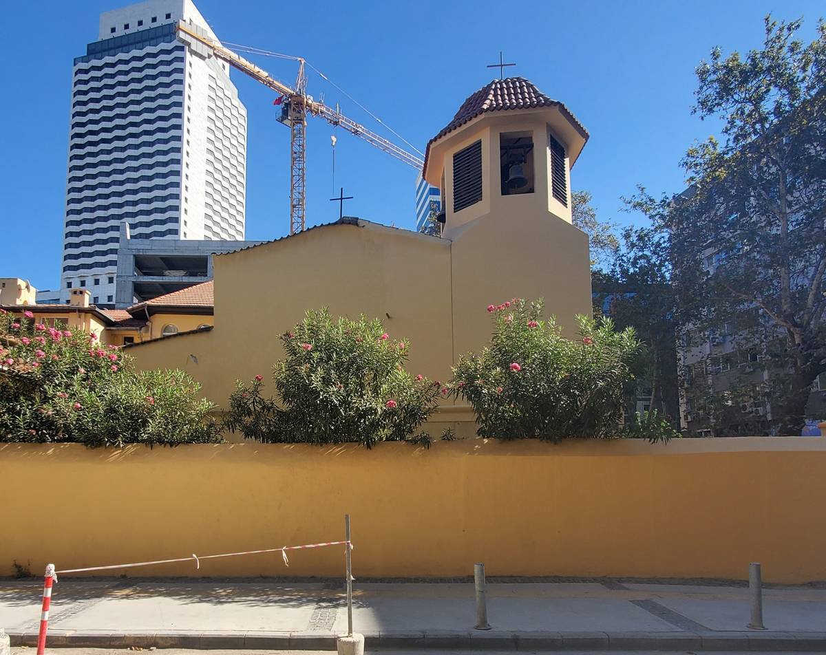 The yellow walls and octagonal bell tower of the church of St. Polycarp in İzmir, among the office towers of the modern city