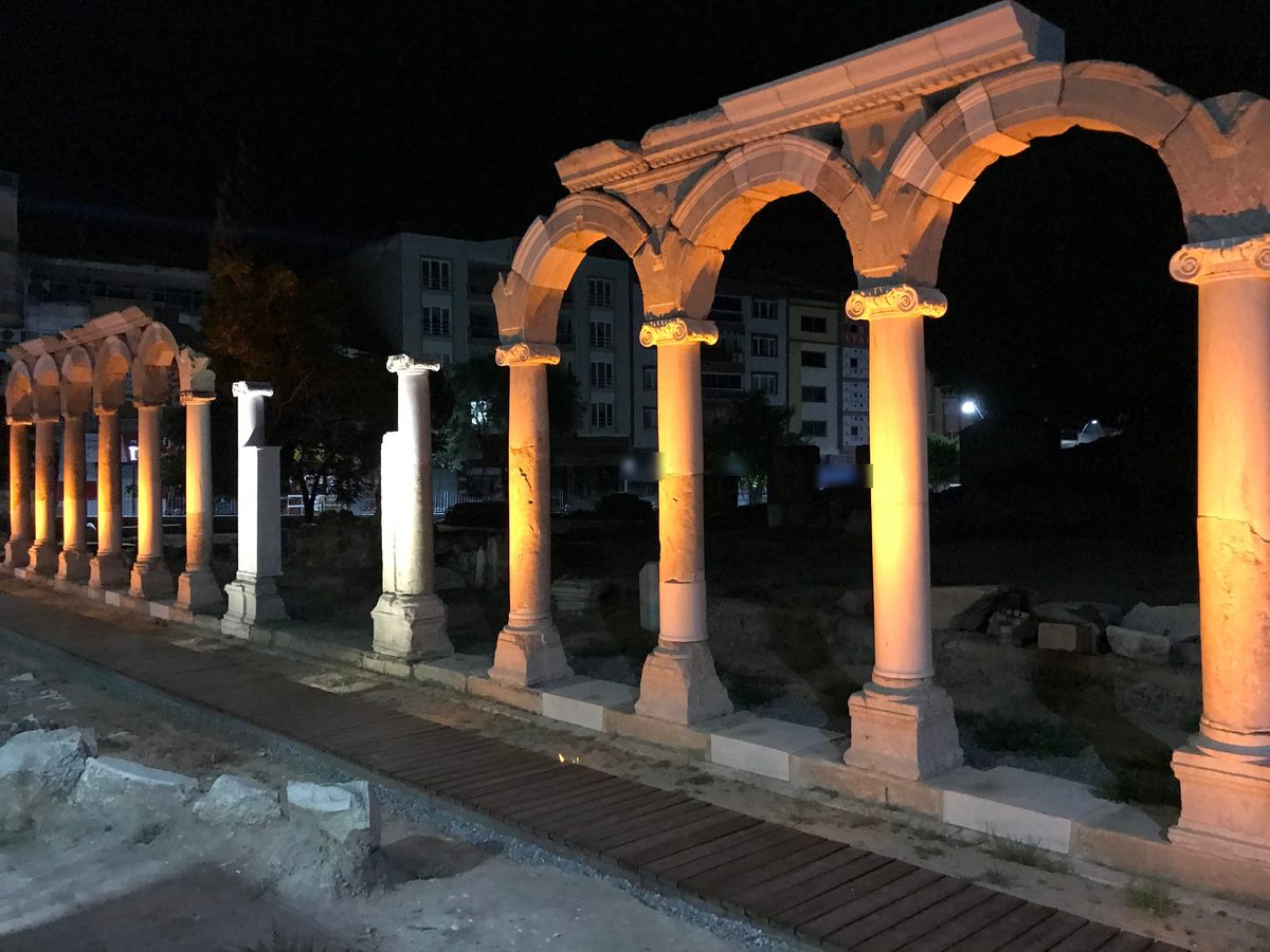 Re-erected columns and arches of the Roman colonnaded street at Thyatira, lit at night, with the apartment blocks of Akhisar behind